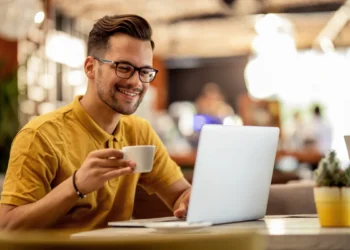 homem-sorridente-navegando-na-net-no-laptop-enquanto-bebe-cafe-quanto-custa-um-dominio-de-site